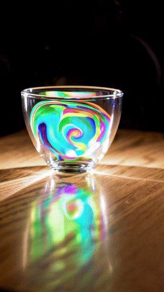 A glass teacup fills itself with swirling liquid light. With warm spotlighting with a subtle tracking shot.